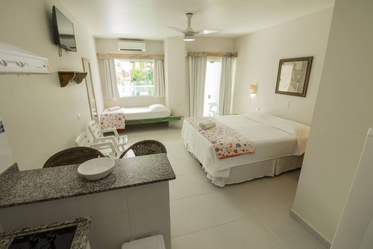 Habitación de hotel con cama, un pequeño escritorio con silla, televisión y ventana con cortinas.