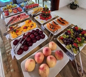 A buffet with various fruits and vegetables, including watermelon, grapes, and peaches. - Apart Hotel Porto Kanoas (Bertioga)