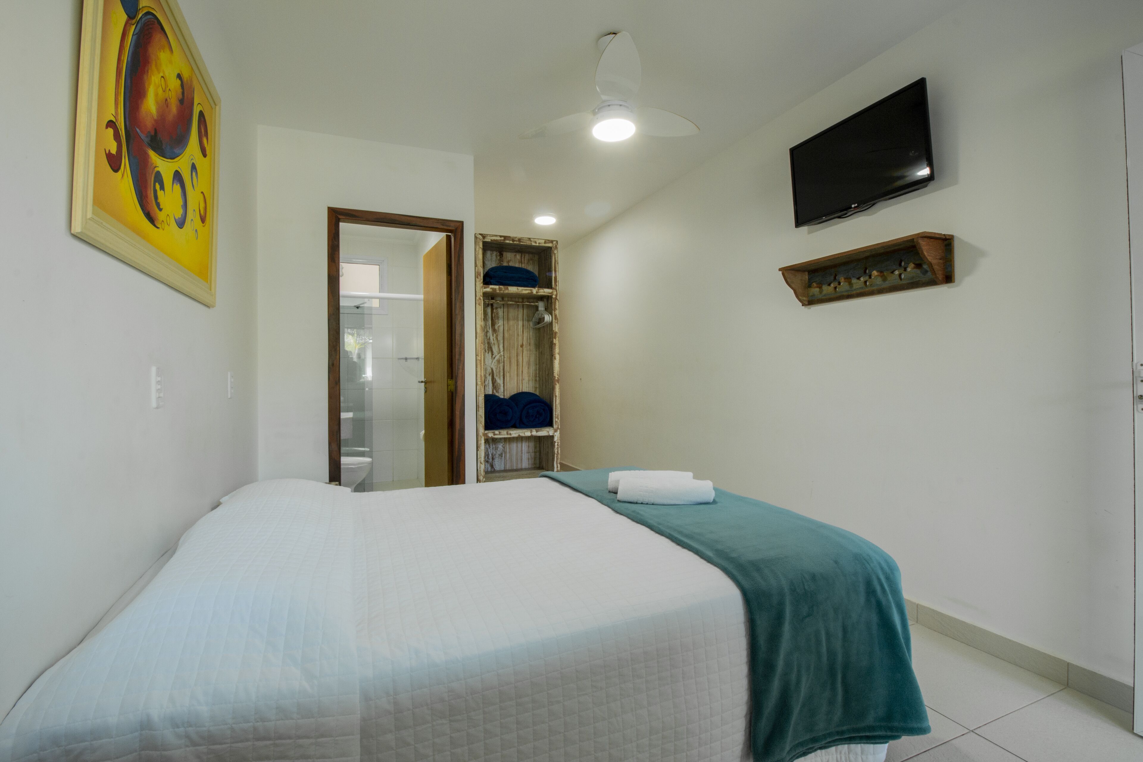 Un dormitorio con cama, televisión, ventilador de techo y un cuadro en la pared.
