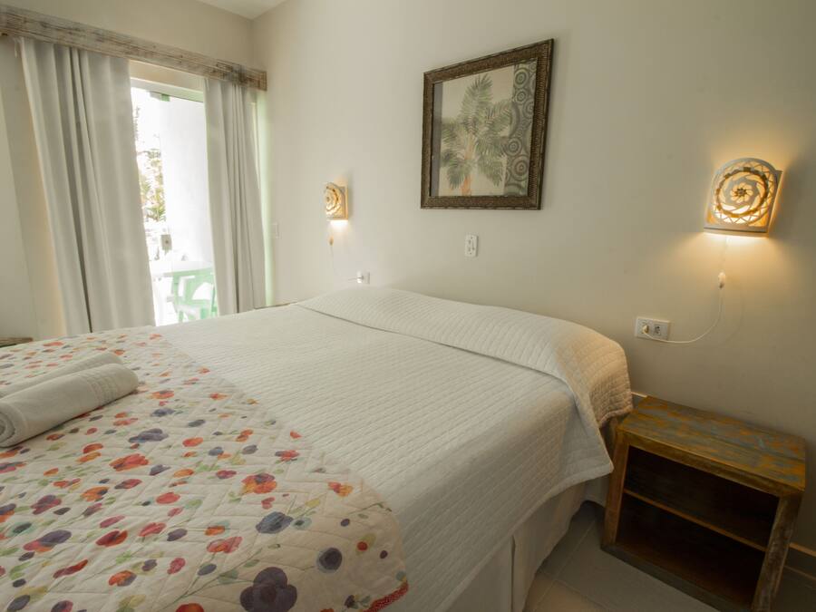 A neatly made bed with a floral-patterned bedspread, a small bedside table with a lamp, and a framed picture on the wall.