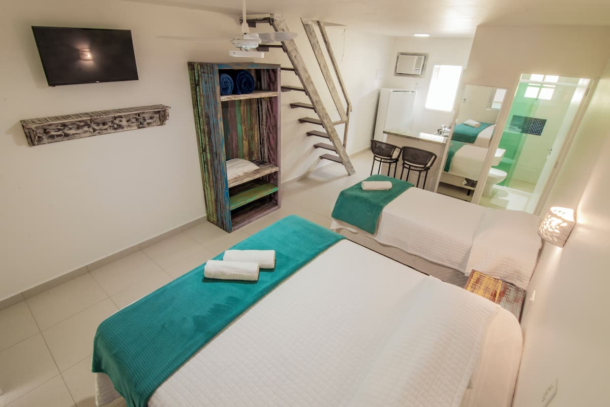 Habitación de hotel con dos camas, un televisor, una escalera de madera, un escritorio y un baño.