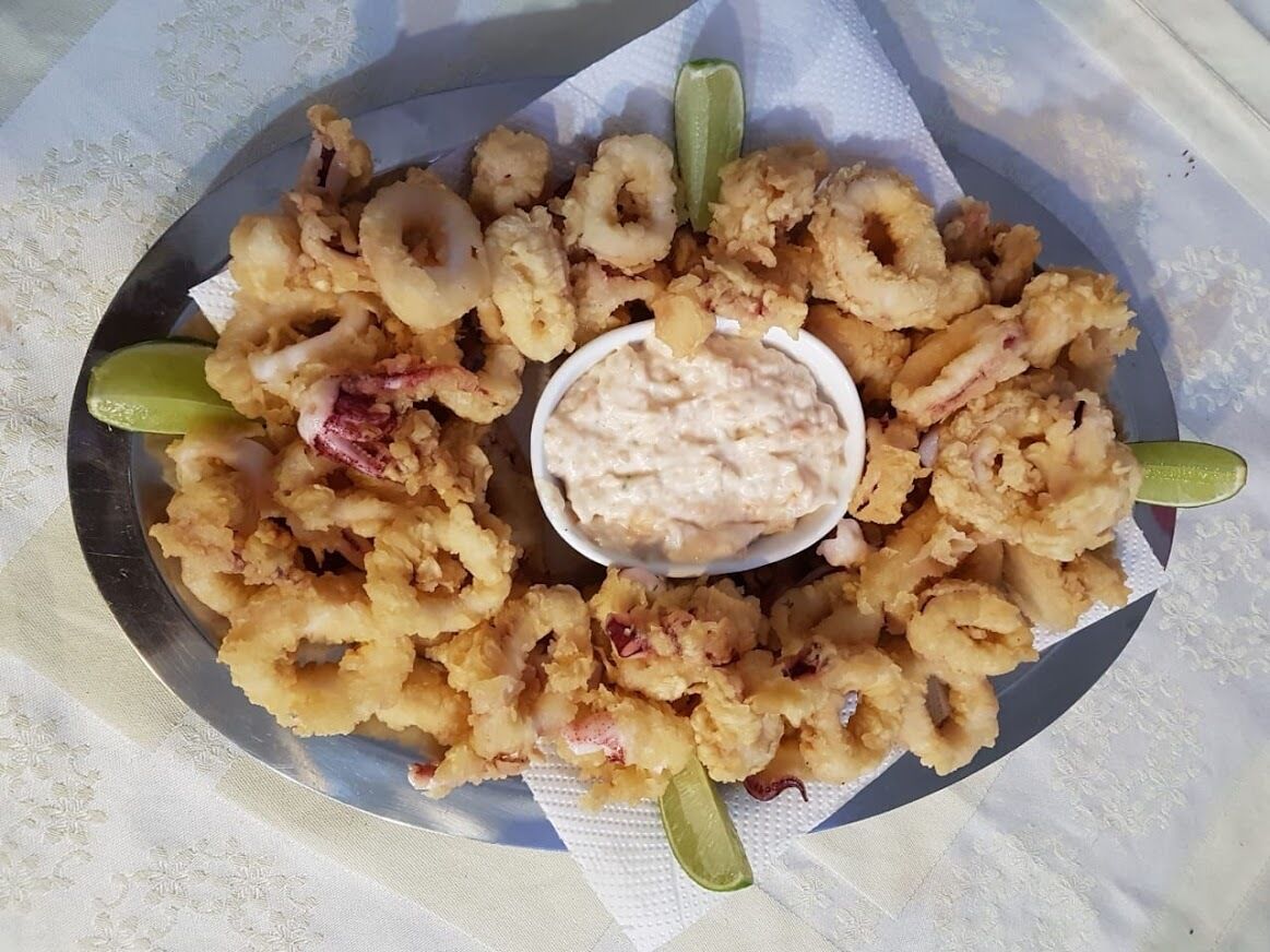 A plate of fried calamari with lemon wedges and a bowl of dipping sauce.