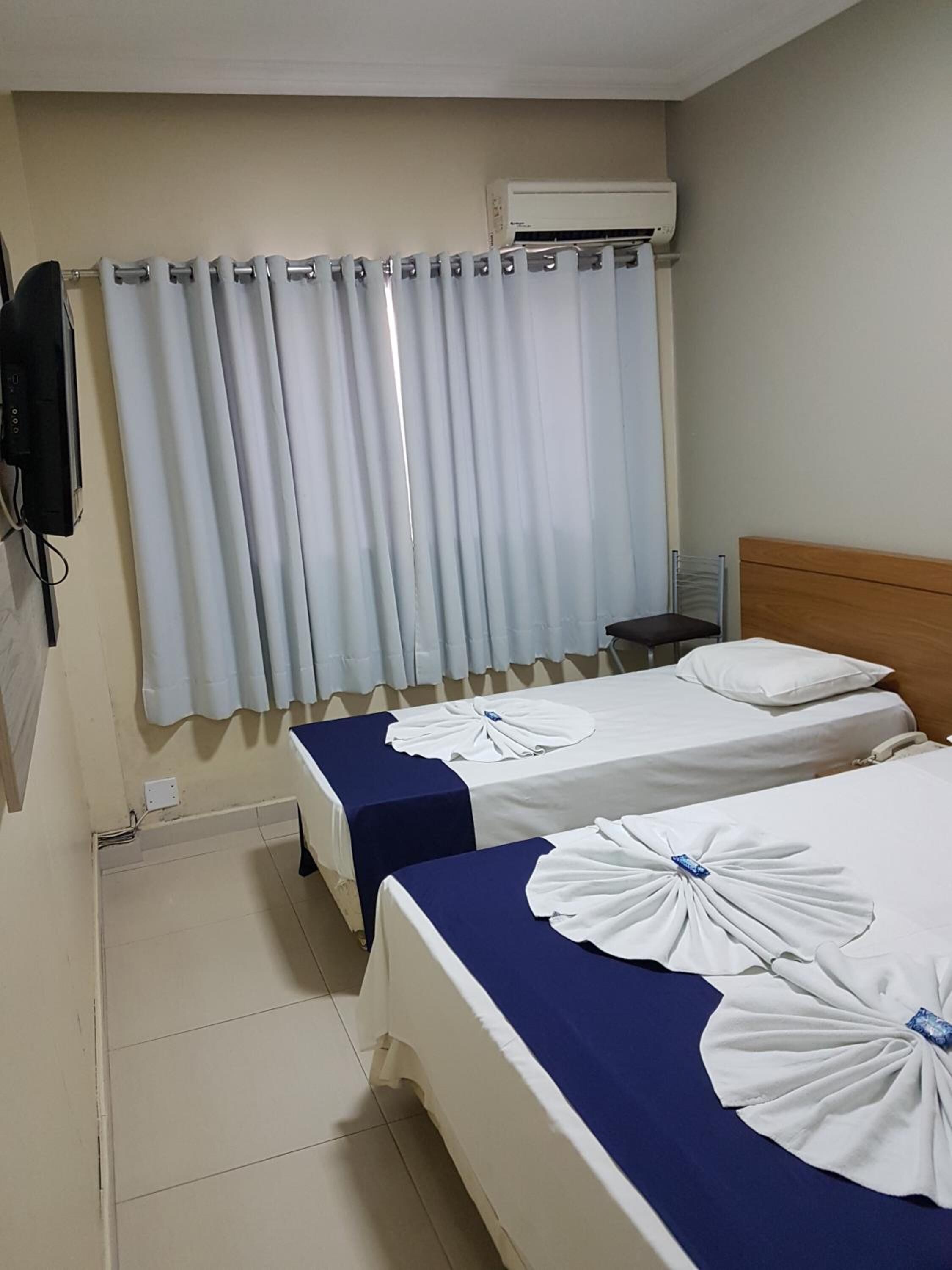 Una habitación de hotel con dos camas, ventilador de techo, aire acondicionado y cortina.