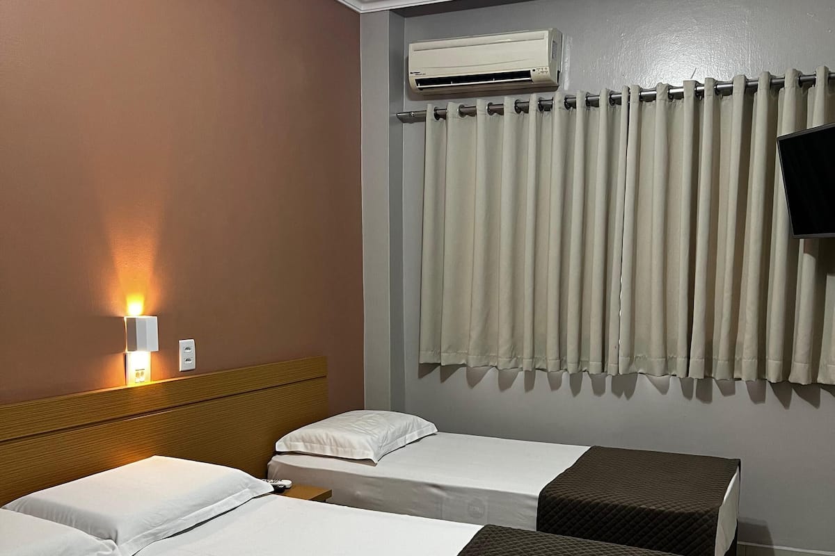 Une chambre d’hôtel avec deux lits, un climatiseur fixé au mur, un rideau et un téléviseur fixé au mur.
