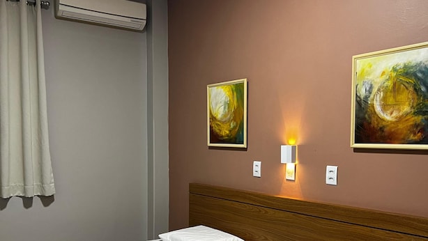 Une chambre d’hôtel avec deux lits simples, un climatiseur fixé au mur, deux tableaux et une lampe de chevet.