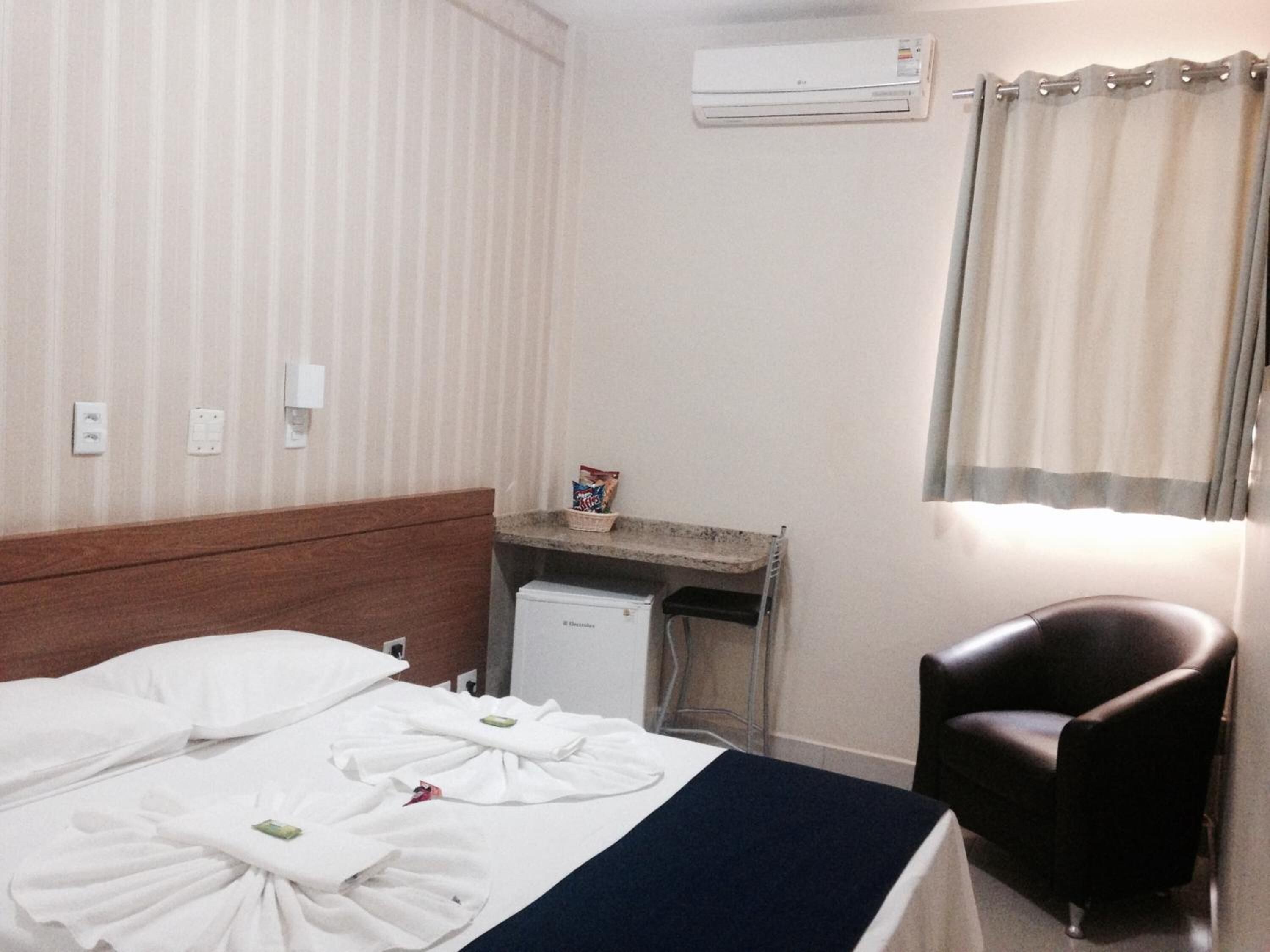 A hotel room with a bed, a desk, a chair, an air conditioner, and a window with curtains.