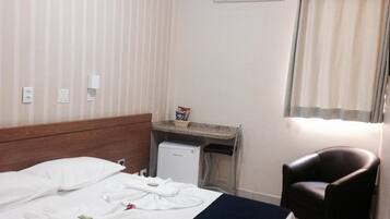 A hotel room with a bed, a desk, a chair, an air conditioner, and a window with curtains.