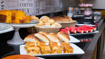 Buffet com diversos alimentos, incluindo bolos, doces e pães.