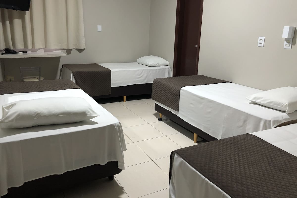 Une chambre d’hôtel avec trois lits, un bureau, une chaise et un téléviseur.