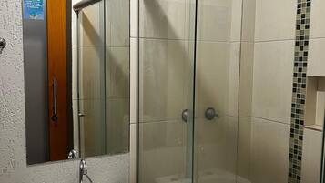 Un baño con ducha de vidrio, un lavamanos blanco y un espejo.