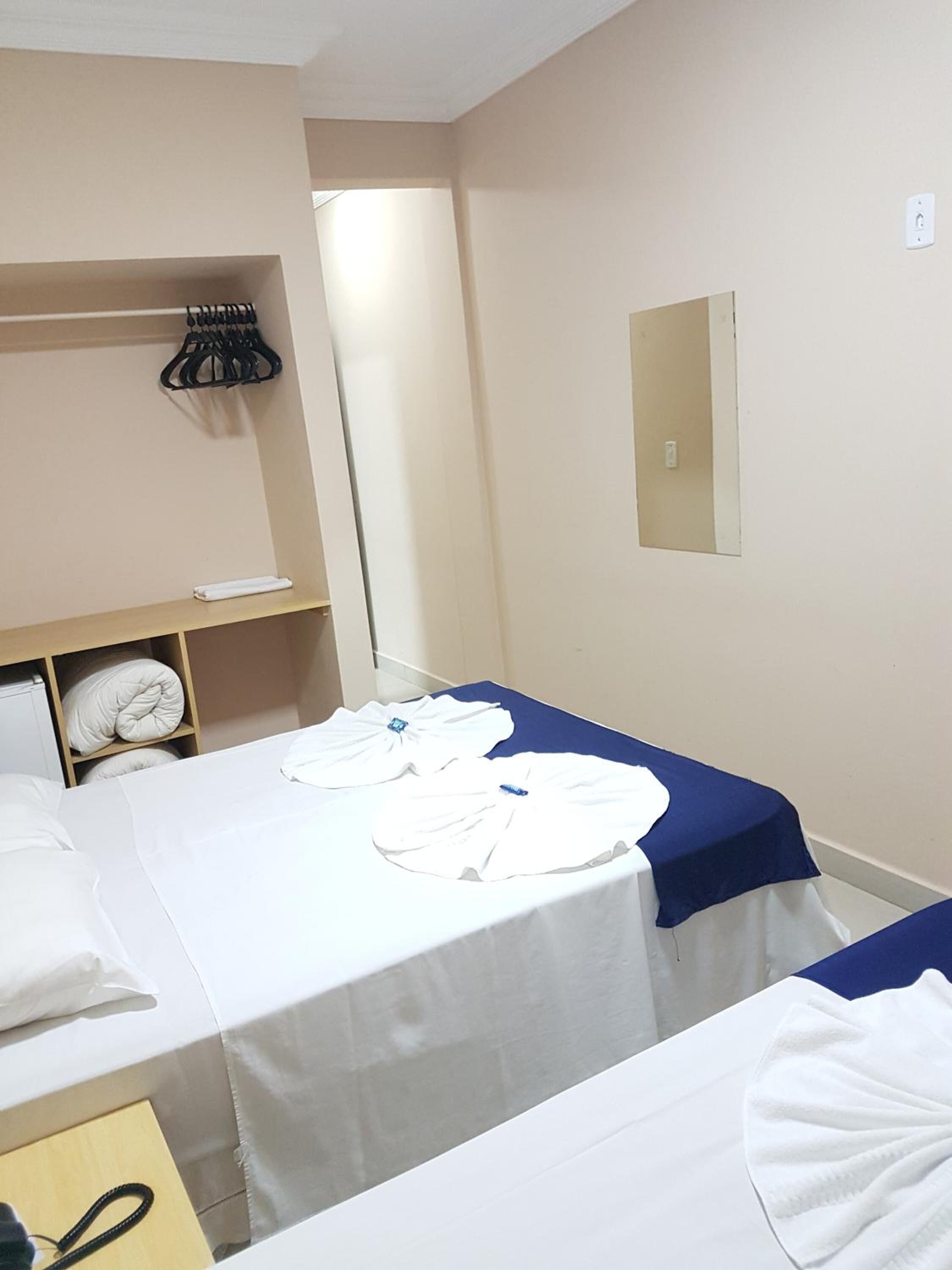 Ett hotellrum med två sängar, en liten hylla med hopvikta handdukar, en spegel och en dörr som leder till ett annat rum.