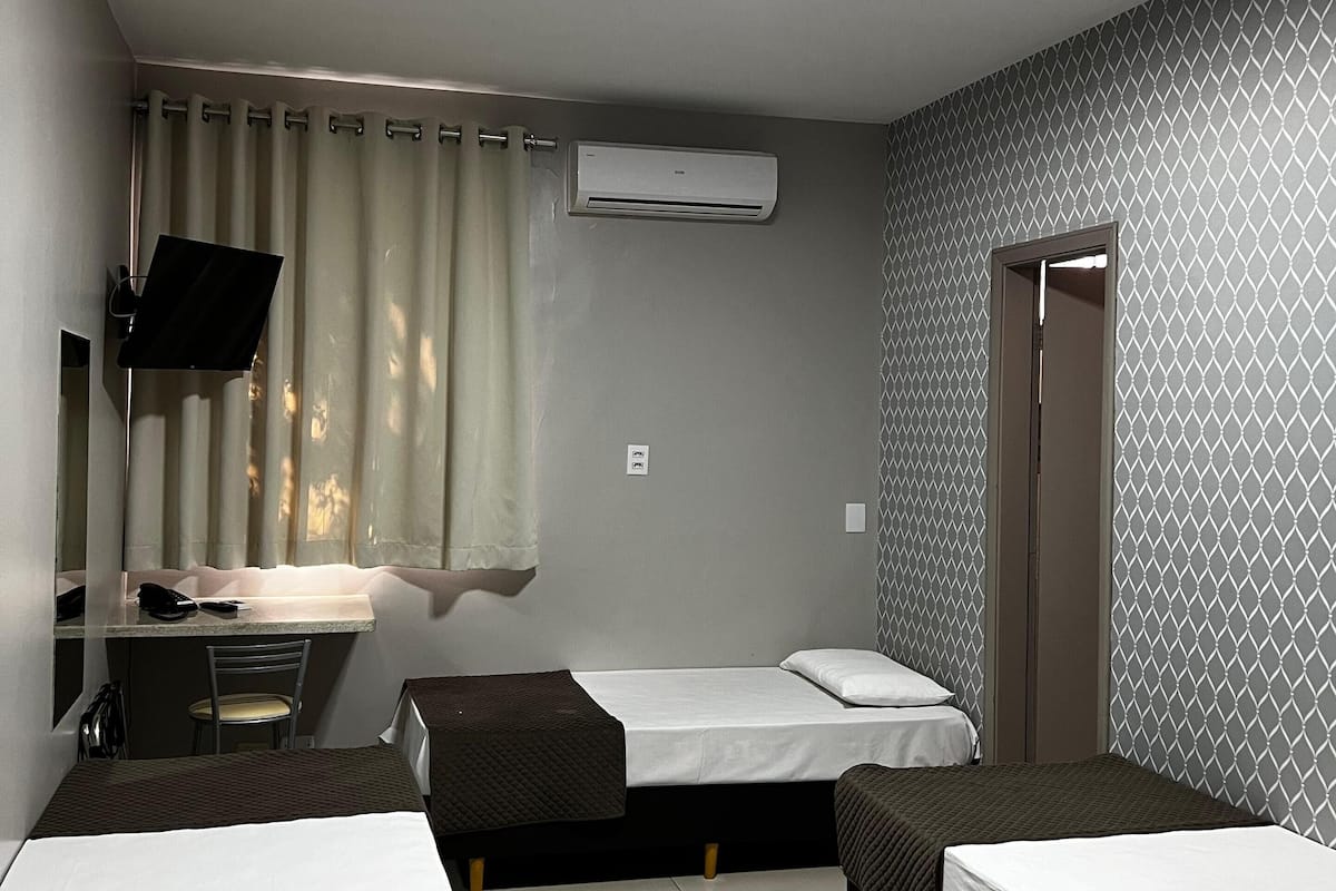 Une chambre d’hôtel avec deux lits simples, un bureau avec une chaise, un téléviseur à écran plat, un appareil de climatisation et une porte de salle de bain.