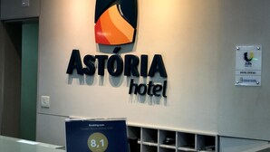 Un comptoir d’accueil avec une enseigne indiquant « Astoria Hotel », une plaque commémorative récompensant l’hôtel par Booking.com, et une enseigne « JUBs ».