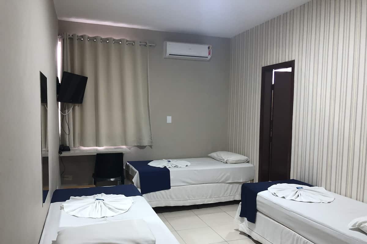 Une chambre d’hôtel avec deux lits simples, un bureau avec une chaise, un appareil de climatisation et un téléviseur fixé au mur.