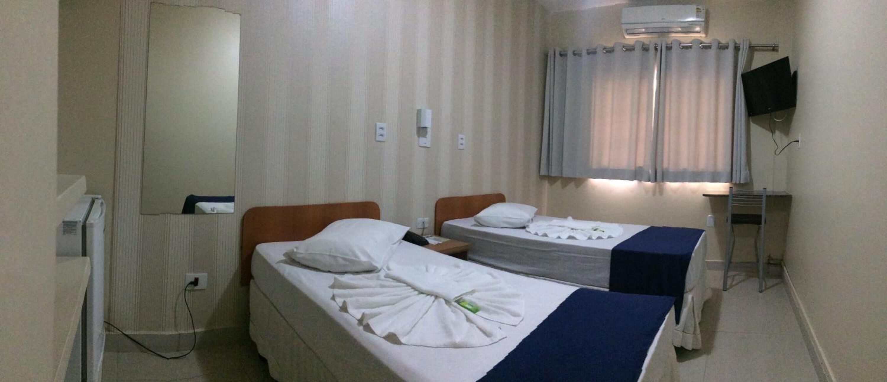 A hotel room with two single beds, a TV, an air conditioner, and a window with curtains.