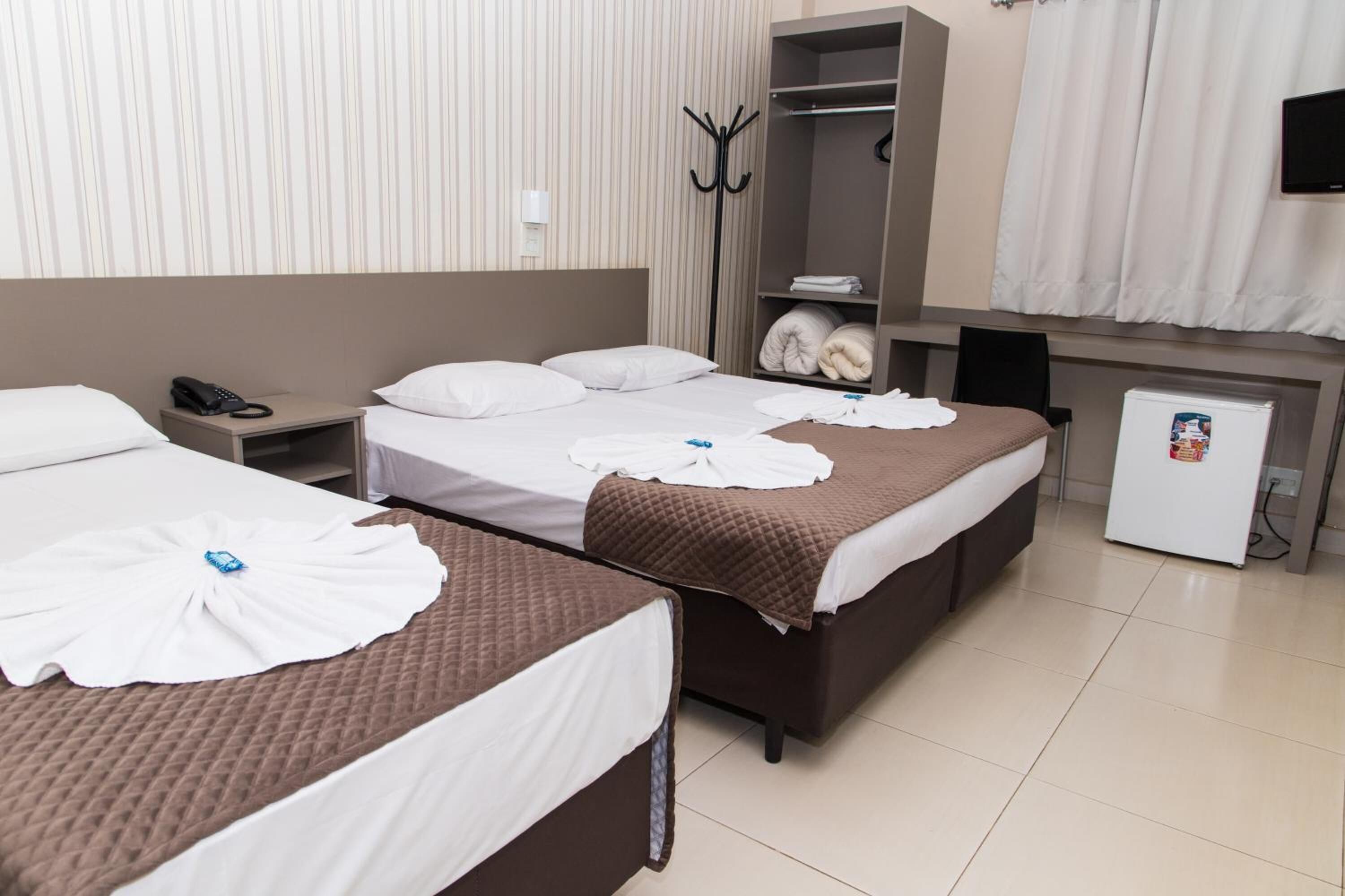 A hotel room with two beds, a wardrobe, a coat rack, a telephone, and a small refrigerator.