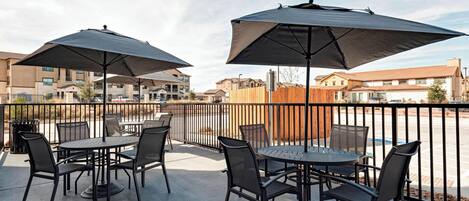 A patio area with round tables and chairs, two large umbrellas, and a view of surrounding buildings.