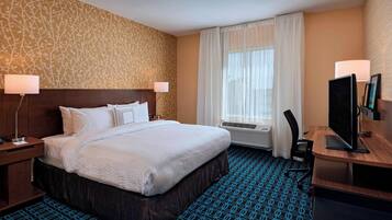 A hotel room with a large bed, a desk with a computer, a TV, and a window with curtains.