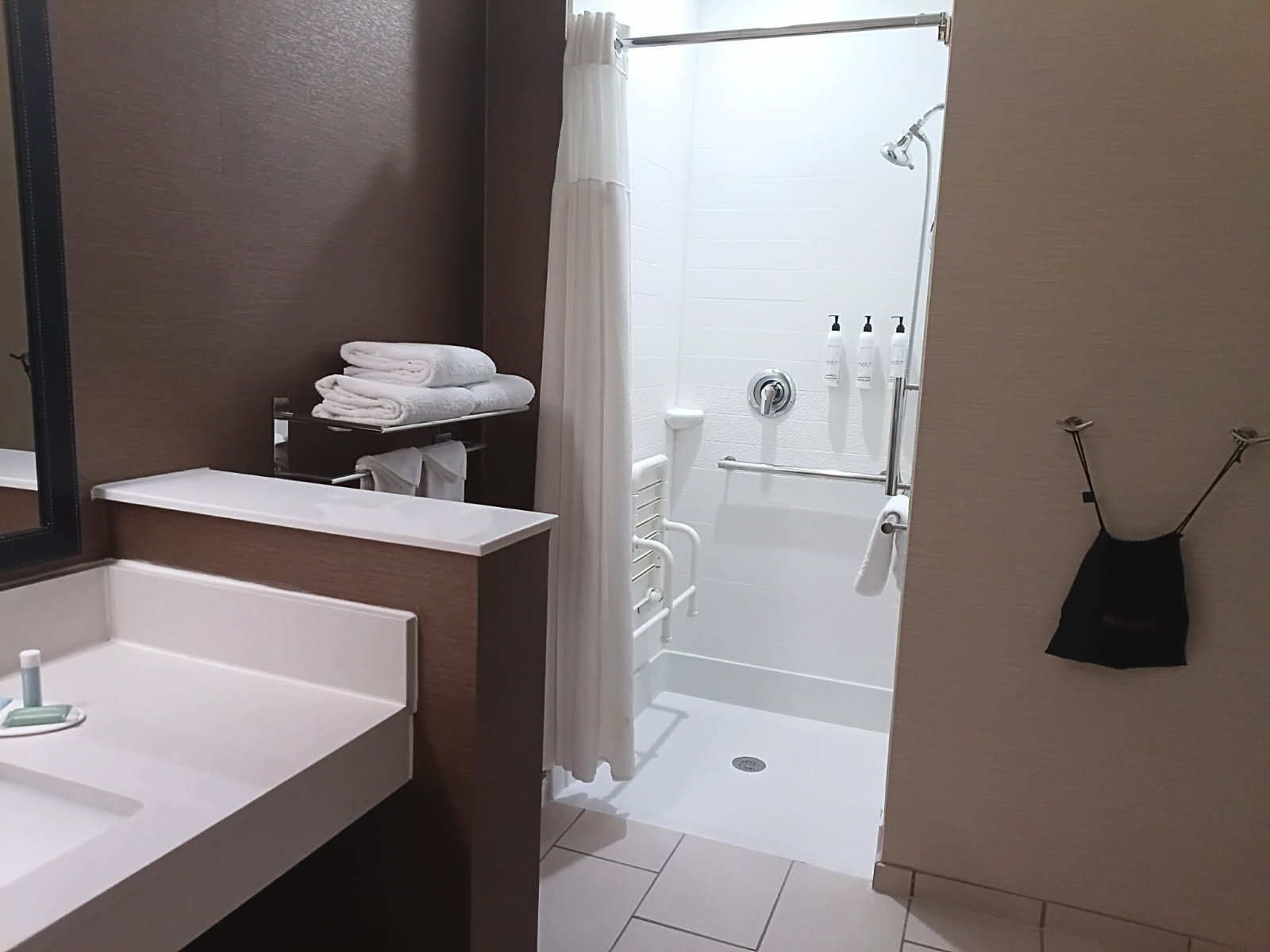 A bathroom with a white sink, a towel rack with folded towels, a shower area with a glass door, and a toilet.