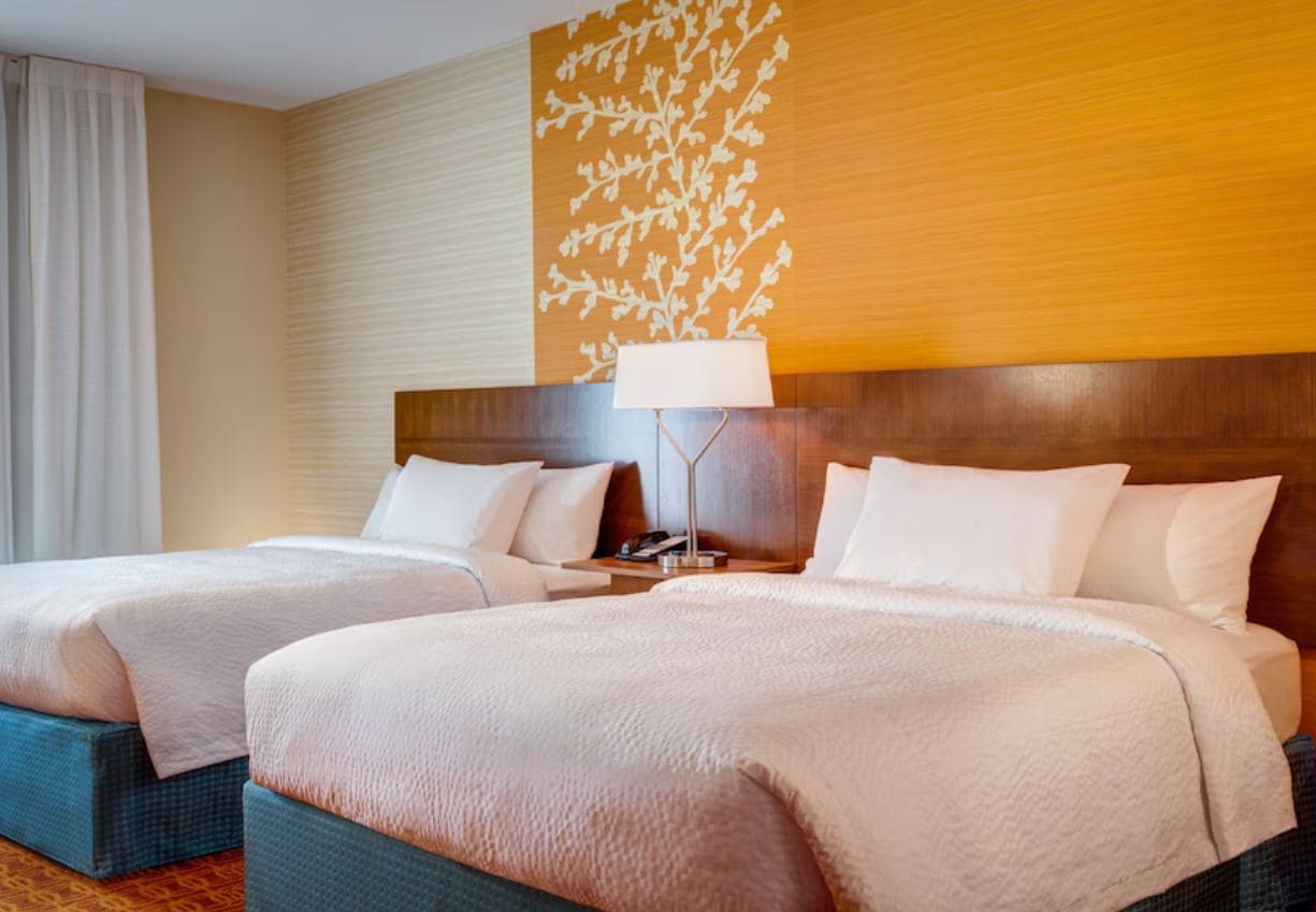 A hotel room with two beds, a nightstand, a lamp, and a wall with a floral pattern.