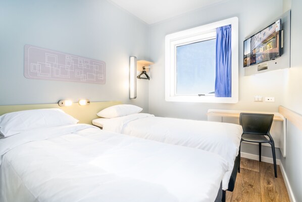 Habitación de hotel con dos camas, un escritorio, una silla, un televisor y una ventana con cortina.