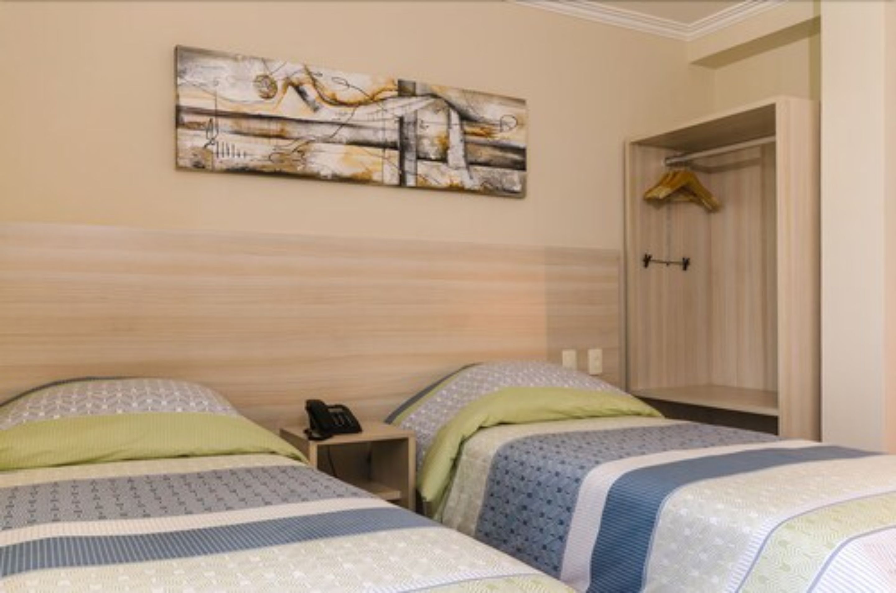 Quarto de hotel com duas camas, mesa de cabeceira com telefone e um quadro na parede.