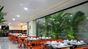 A restaurant with tables set for dining, orange chairs, and a glass wall with a view of palm trees. - Seleto Hotel (Volta Redonda)
