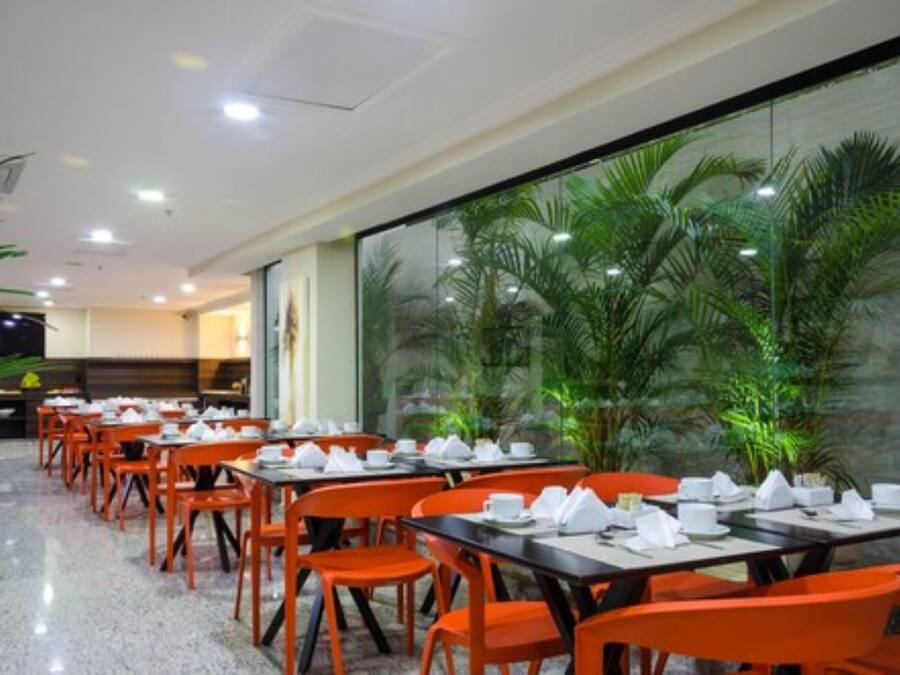 A restaurant with tables set for dining, orange chairs, and a glass wall with a view of palm trees.