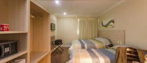 A hotel room with a bed, a desk with a laptop, a microwave, and a refrigerator.