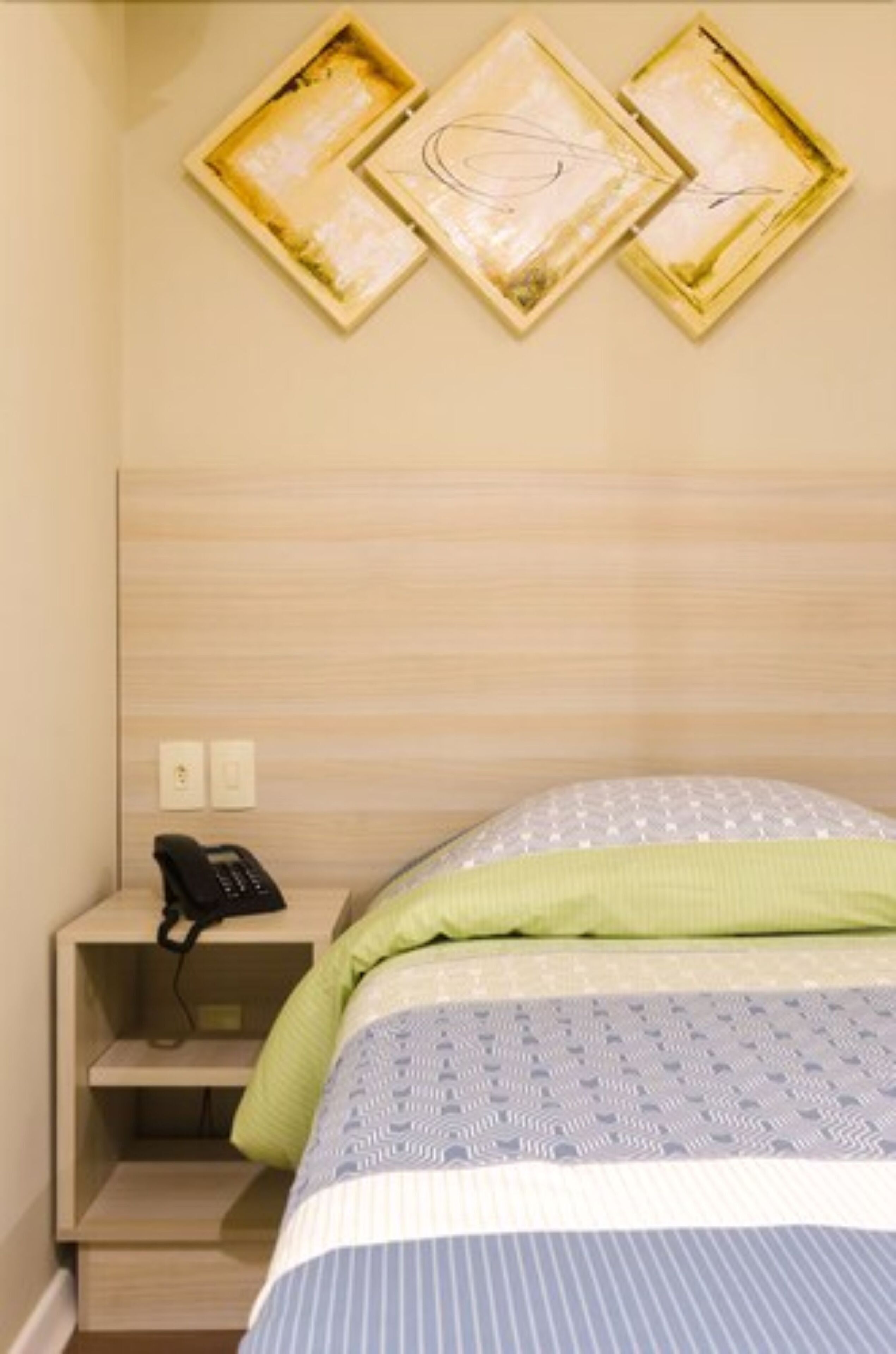 Ein Hotelzimmer mit einem Bett, einem Nachttisch mit Telefon und drei gerahmten Bildern an der Wand.