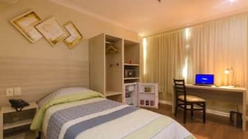 Una habitación de hotel con cama, escritorio con computadora, armario y pequeño mueble.