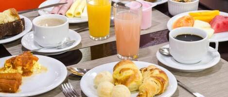 A breakfast setting with plates of food, including croissants, bread, and fruit, along with beverages like orange juice and coffee.