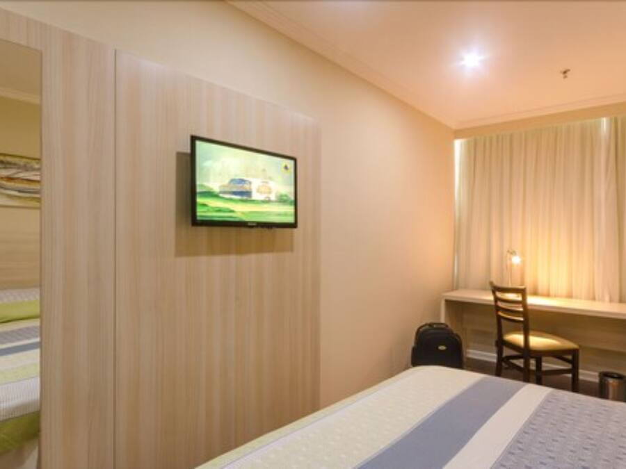 A hotel room with a bed, a desk, a chair, a television, and a window with curtains.