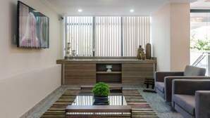 A modern living room with a sofa set, a coffee table with a plant, and a large window with blinds. - Seleto Hotel (Volta Redonda)