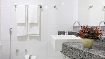 Un baño moderno con azulejos blancos, un lavamanos blanco, un espejo y una planta en maceta sobre el mostrador.