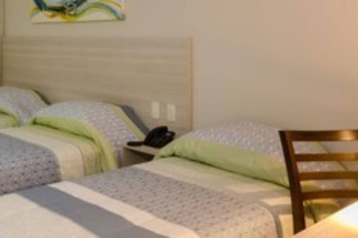 Ein Hotelzimmer mit zwei Betten, einem Nachttisch, einem Sessel und einem Schreibtisch mit einer Lampe.