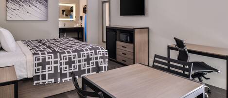 Habitación de hotel con cama, escritorio, silla, televisión, microondas y espejo.