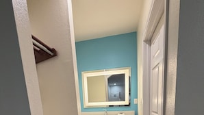 A narrow hallway leading to a bathroom with a mirror, sink, and towel rack. - Crystal Inn & Suites IAH Humble (Humble)