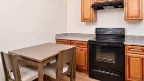 A small kitchen with a wooden table and chairs, a black stove, and wooden cabinets. - Crystal Inn & Suites IAH Humble (Humble)