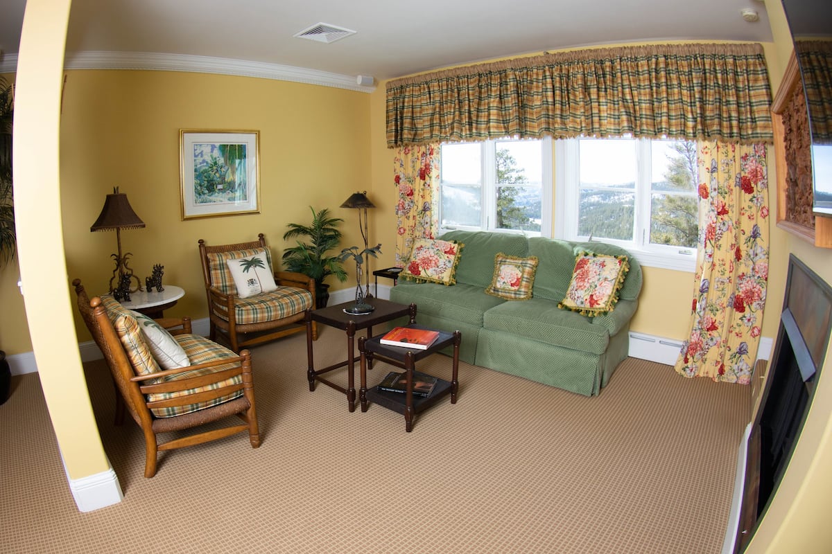 A cozy living room with a green sofa, a wooden armchair, a small table, and a floor lamp.