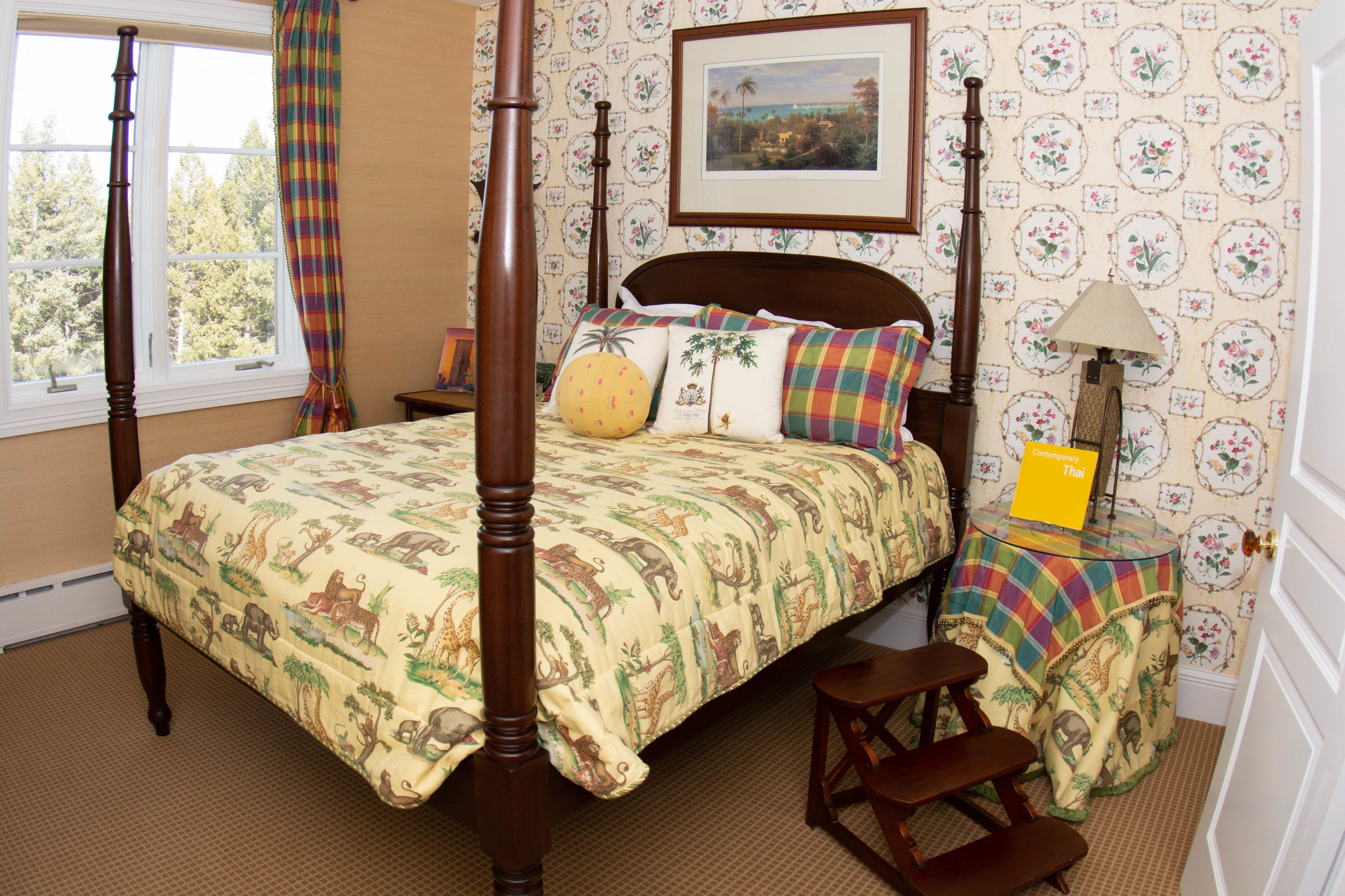Una cama con dosel con colcha estampada, una mesita de noche con lámpara, y un cuadro en la pared.