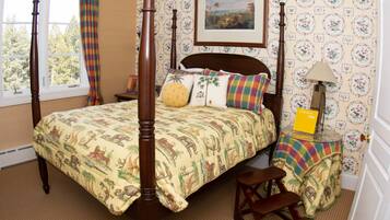 Una cama con dosel con colcha estampada, una mesita de noche con lámpara, y un cuadro en la pared.