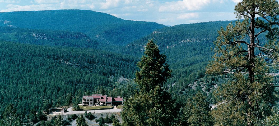 A house surrounded by dense forest with a mountainous backdrop.