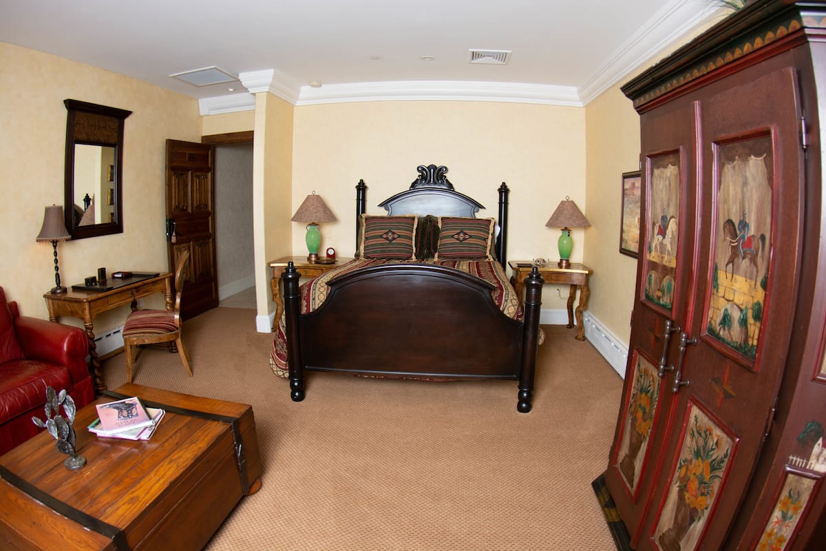 A bedroom with a large bed, a wooden dresser, a red leather chair, a wooden coffee table, and a desk with a lamp.