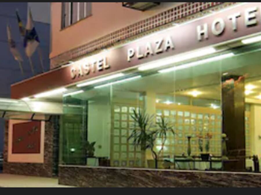 Exterior del hotel Castel Plaza, con fachada de vidrio, zona de estar al aire libre y un cartel.