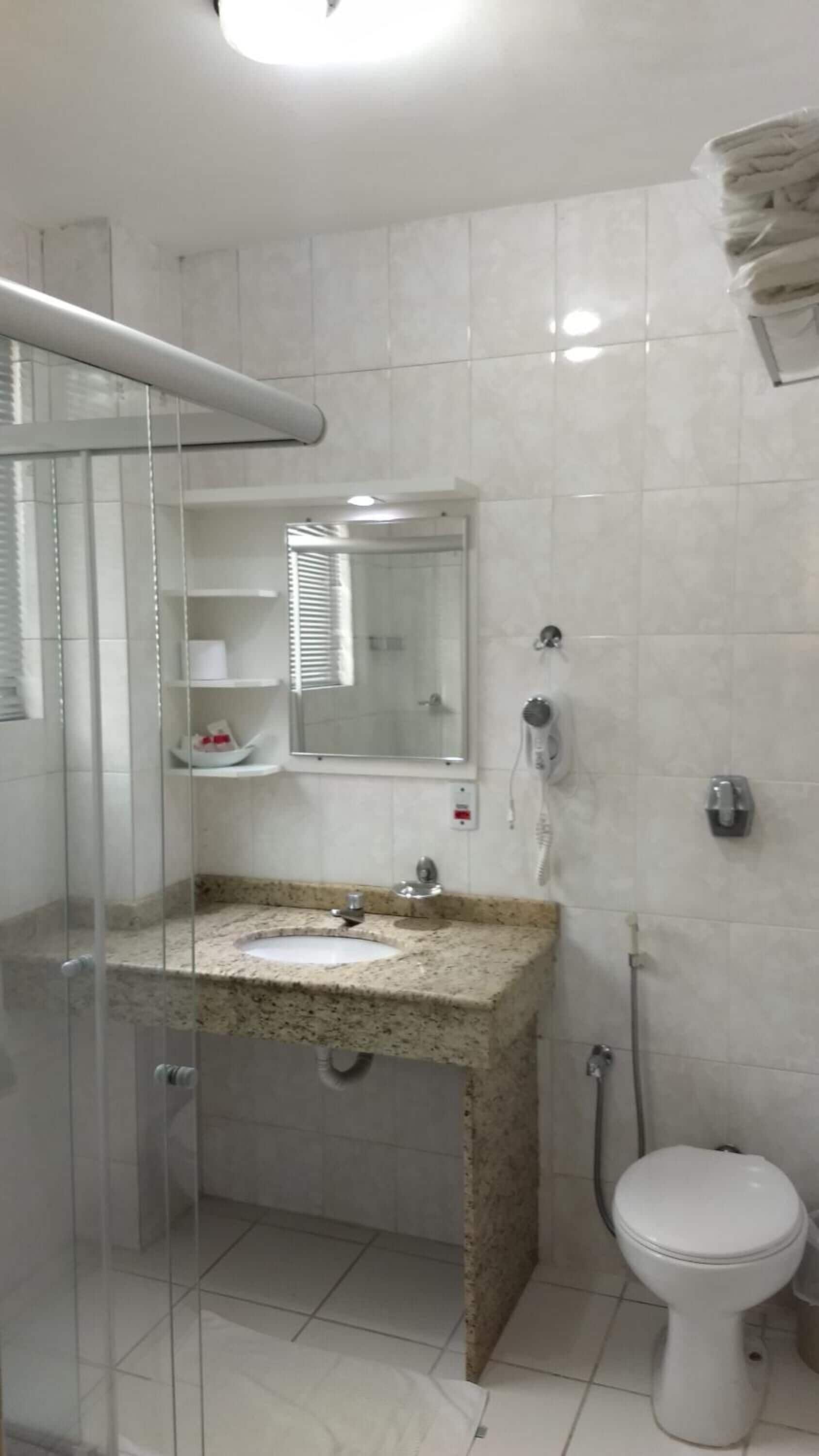 Une salle de bain avec une douche à parois de verre, un lavabo avec un plan de travail en granit, un miroir, des toilettes et un porte-serviettes.