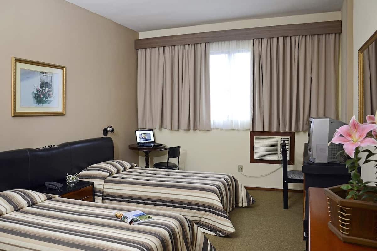 Ein Hotelzimmer mit zwei Betten, einem Schreibtisch mit Computer, einem Fernseher und einem gerahmten Bild an der Wand.