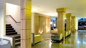 Eine großzügige Lobby mit einer Treppe, hohen Holzsäulen und einer Sitzecke mit einer Couch und Sesseln.