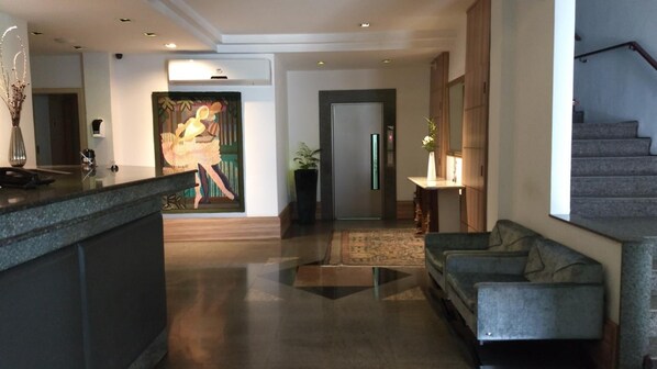 A modern hotel lobby with a reception desk, a large abstract painting, a staircase, and a seating area. - Castel Plaza Hotel (Resende)