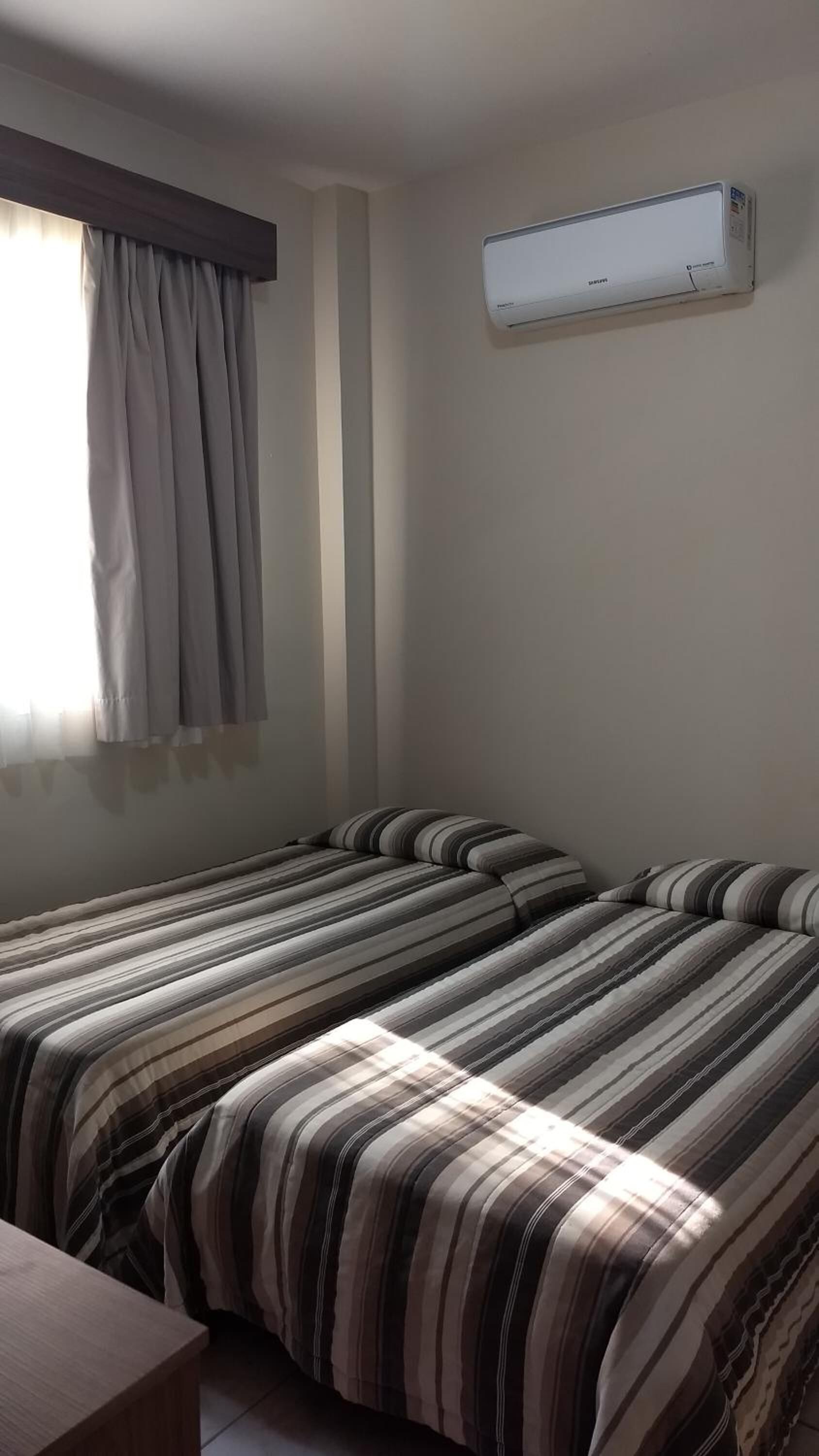 Habitación con dos camas, una ventana con cortinas y un equipo de aire acondicionado en la pared.